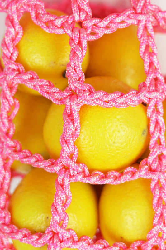Hanging storage bag for fruit or other small items made of paracord rope, this one is in neon pink.
